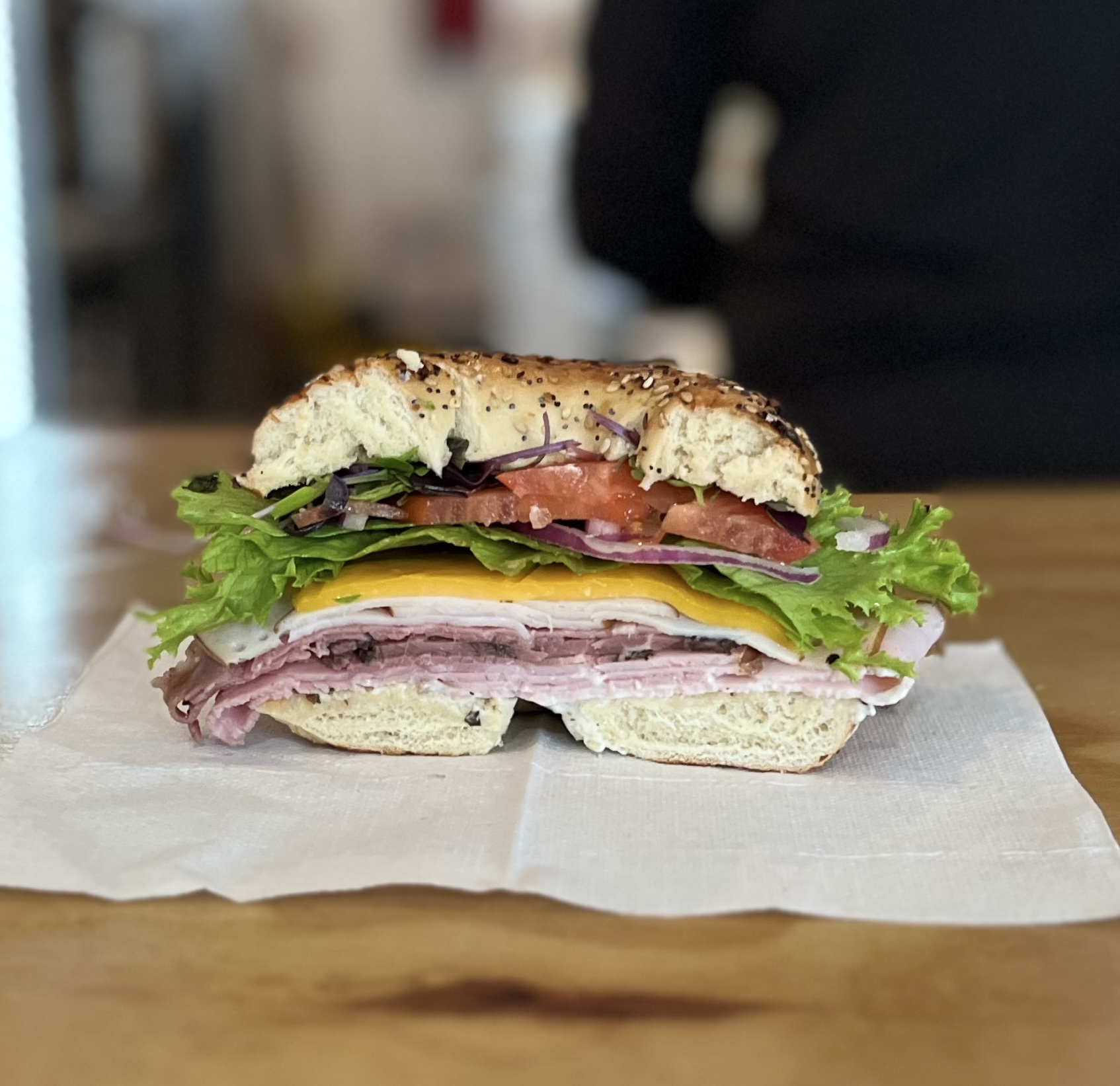 Stacked deli bagel sandwich with ham, turkey, cheese, lettuce, tomato, and onion